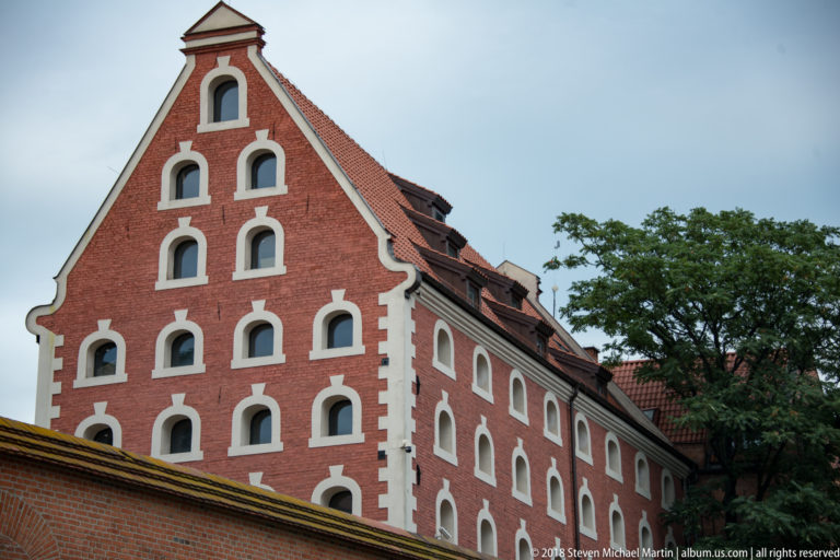 Red-brick historic granary with steep gable and rows of small white-trimmed openings in Toruń.