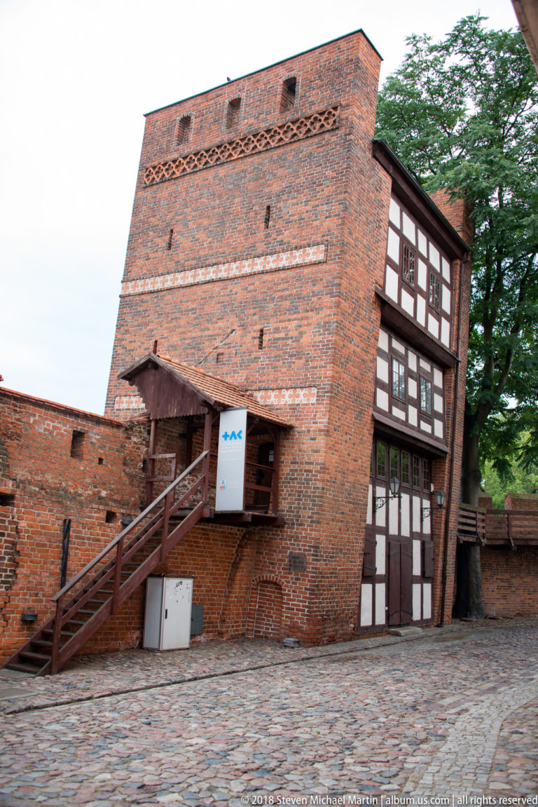 Large brick fortification building with exterior stairs and attached timber-framed wall in Toruń.