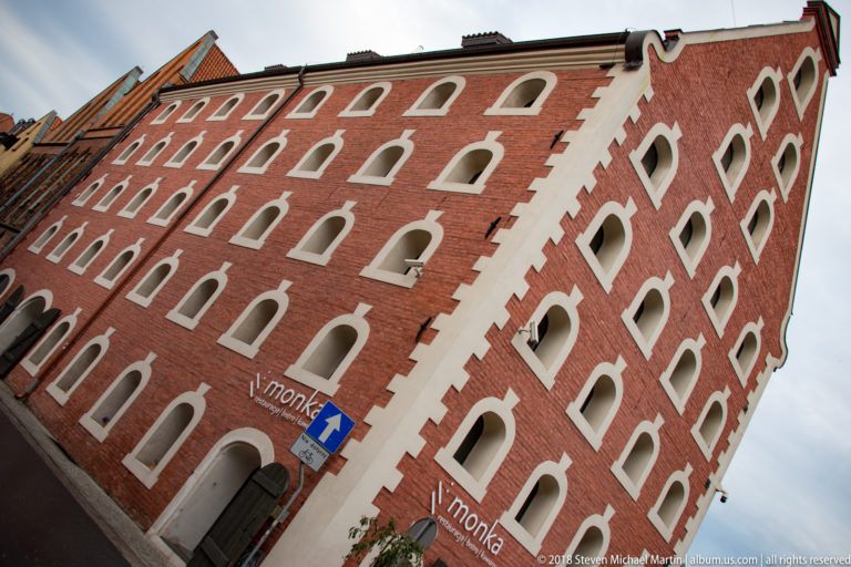 Low-angle view of tall red-brick granary with many white-trimmed openings and steep gable.