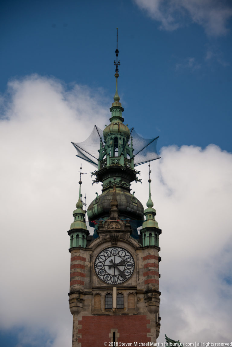 Clock tower of Gdańsk Główny with copper turrets and ornate cupola against blue sky and clouds.