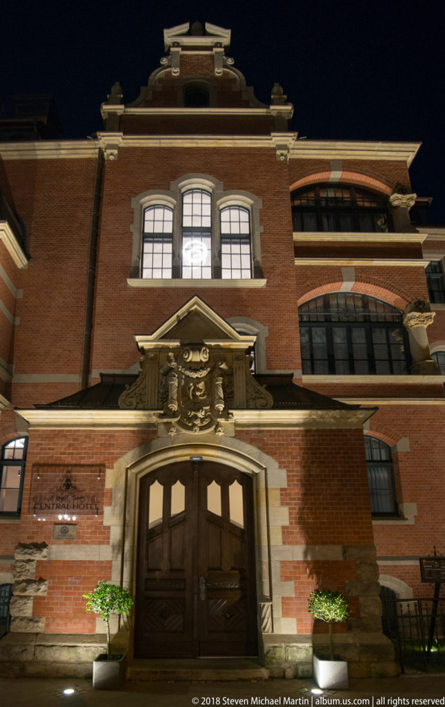 Decorative station doorway with dark wooden doors, carved pale stone surround, heraldic relief, and red-brick façade.
