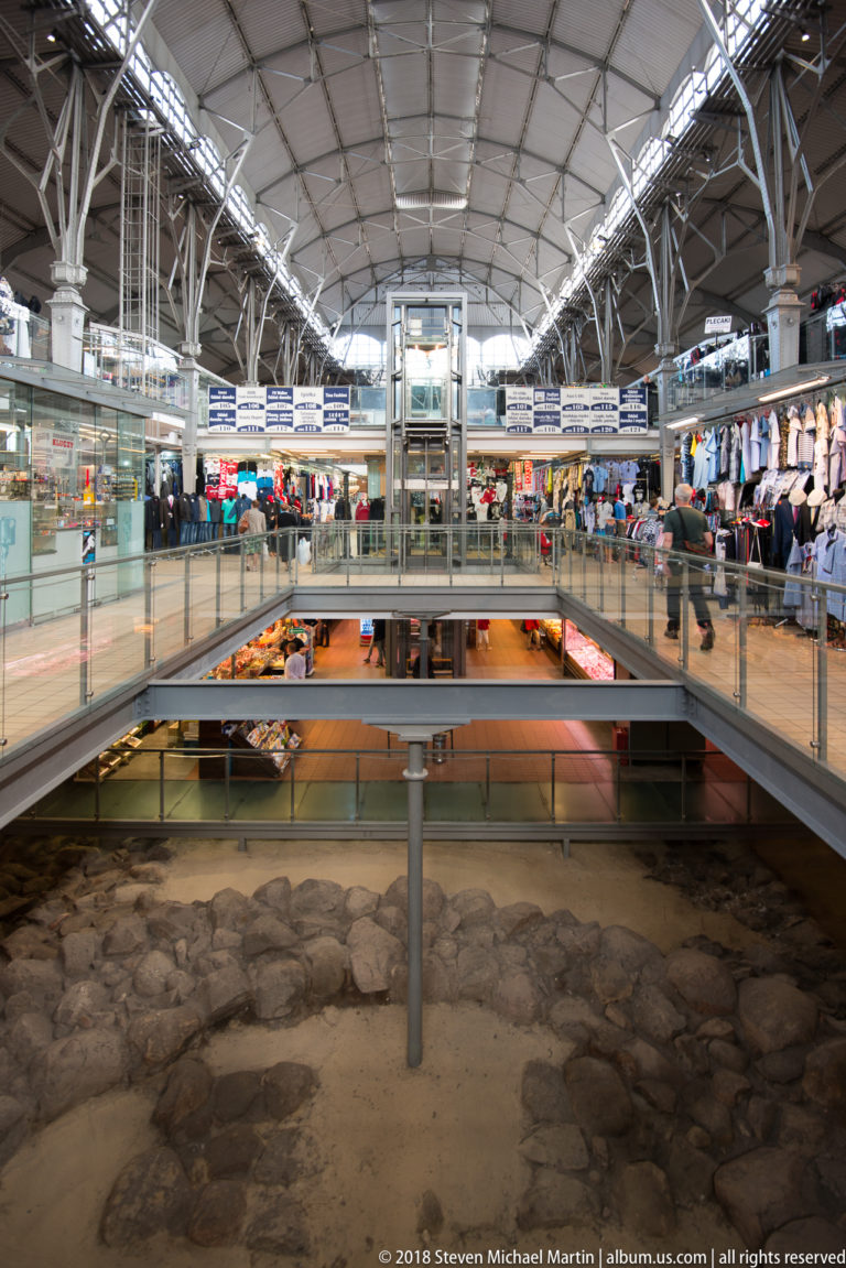 Modern market galleries and elevator above exposed old masonry preserved on the lower floor.
