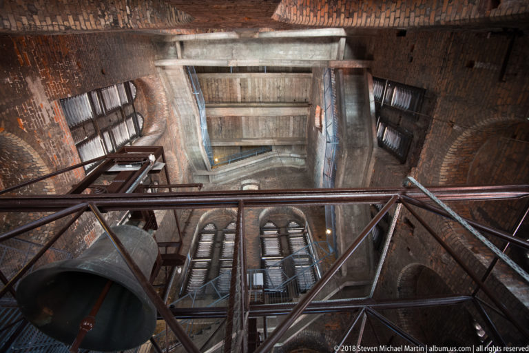 Large bell, metal framing, platforms and brick vaulting seen looking upward inside St. Mary’s Basilica tower.