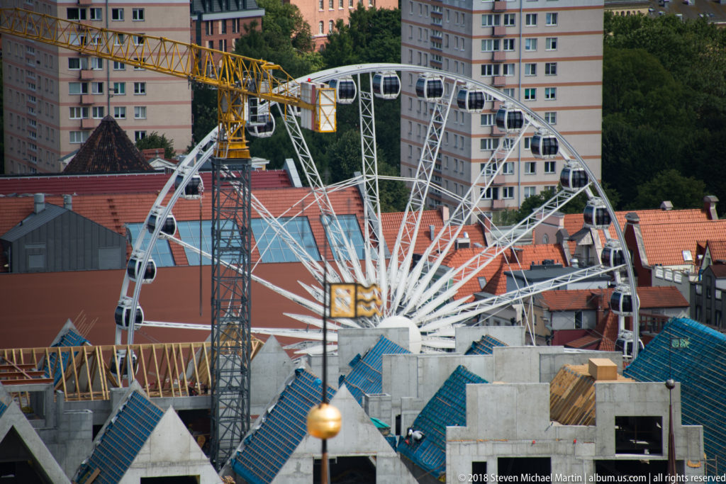 White Ferris wheel above red rooftops, construction cranes and apartment buildings in central Gdańsk.