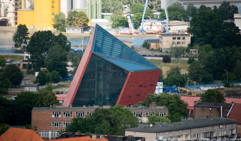 Angular modern red building with large dark-glass façade and steep triangular roof in Gdańsk.