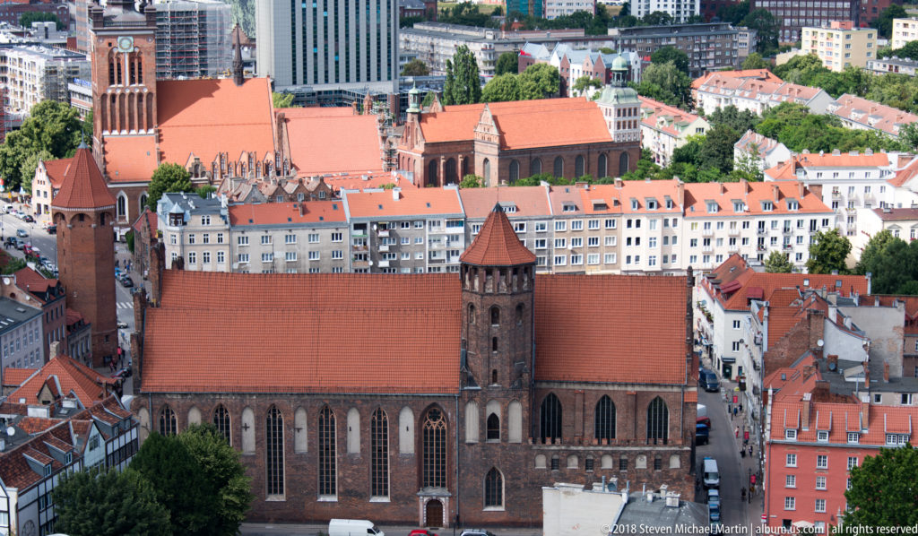 Large Brick Gothic church with steep red roof, pointed windows and square tower seen from above in Gdańsk.