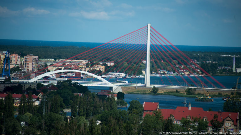 Cable-stayed bridge with tall white pylon and red cables spanning the Martwa Wisła in Gdańsk.