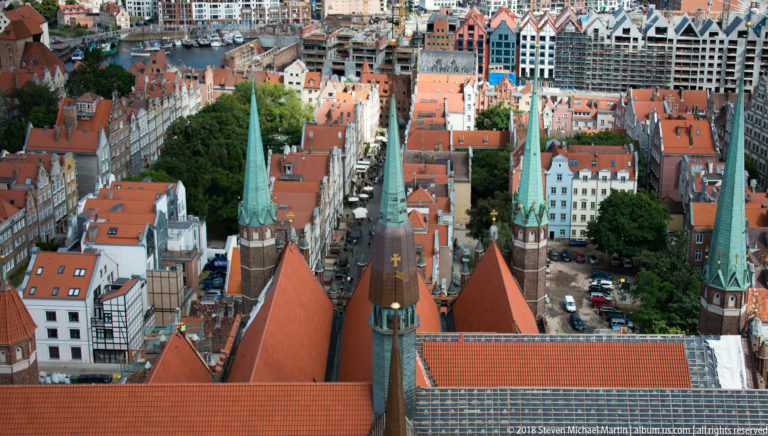 High view over red roofs, narrow streets and green church spires in Gdańsk’s historic center.