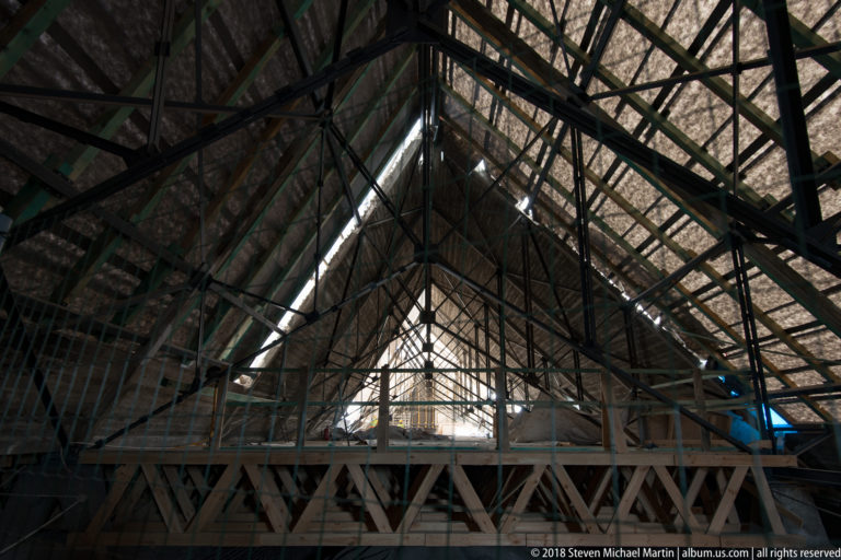 Long view through a steep timber roof with repeated rafters, cross-bracing, and an elevated visitor platform.