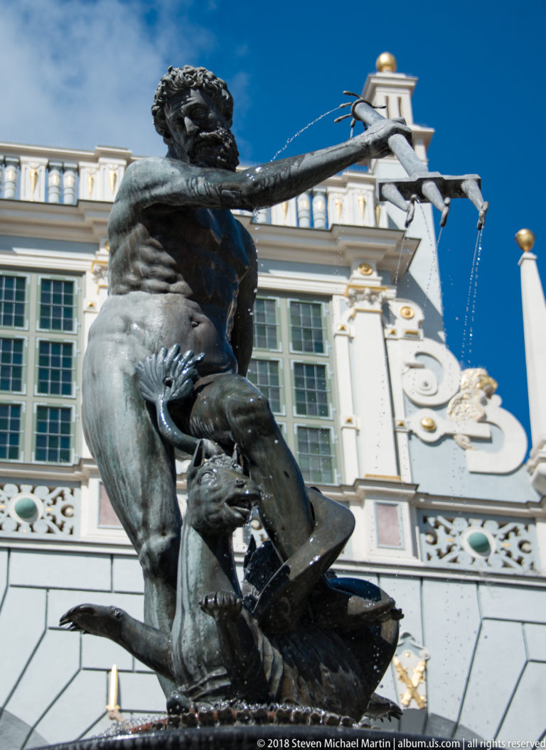 Close view of the bronze Neptune figure holding a trident above a sculpted sea creature.