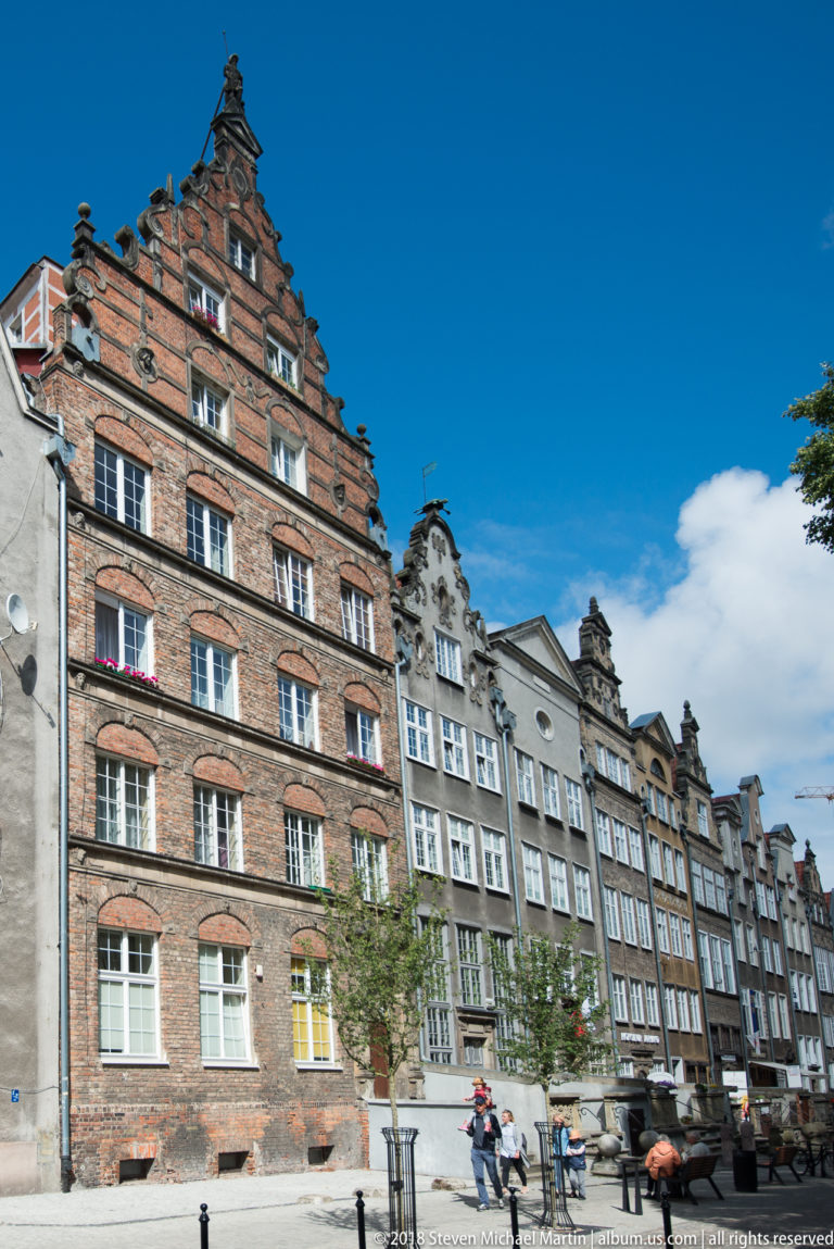 Historic Gdańsk street lined with narrow brick and stucco houses topped by stepped and curving gables.