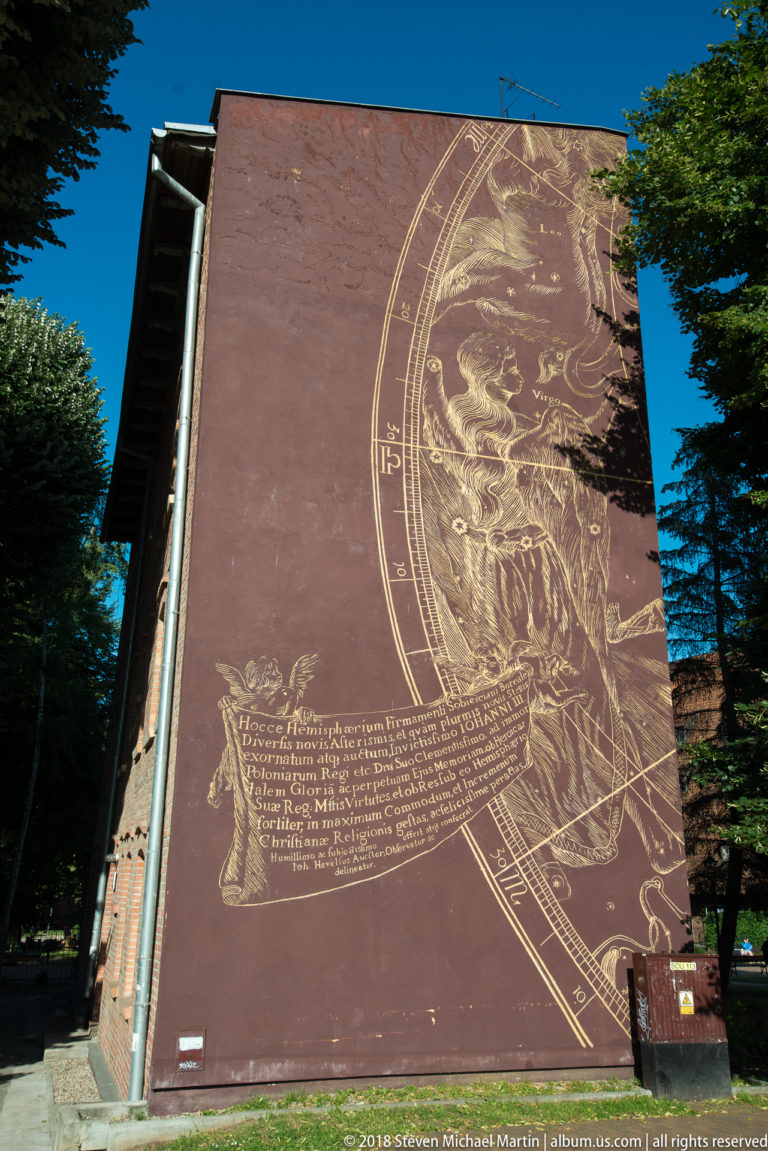 Exterior mural with a partial circular celestial diagram, illustrated figures, fine linework, and a long historical inscription.
