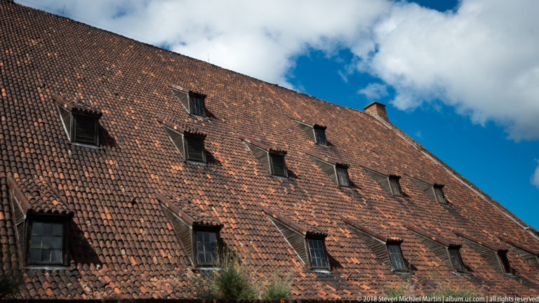 Steep weathered red clay-tile roof with multiple rows of small dark dormer windows.