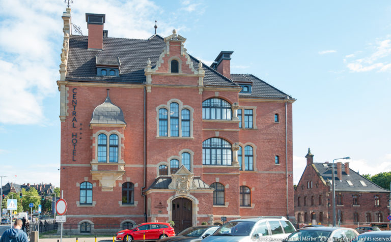 Historic red-brick Central Hotel with gables, bay windows, pale stone trim, and cars parked along the street.