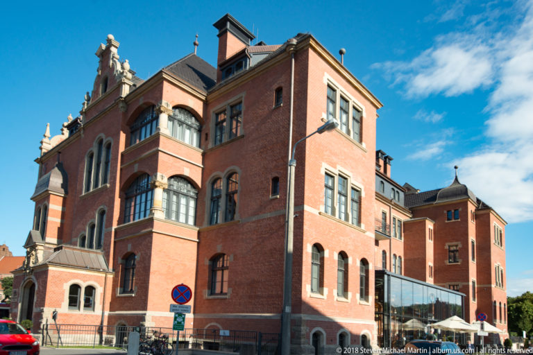 Oblique side view of the red-brick Central Hotel with tall windows, projecting bays, and a modern glazed addition.