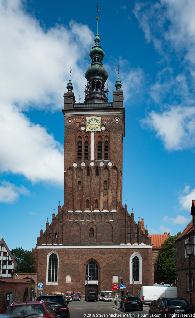 Massive square brick church tower with clock, arched openings, stepped gables and green cupola.