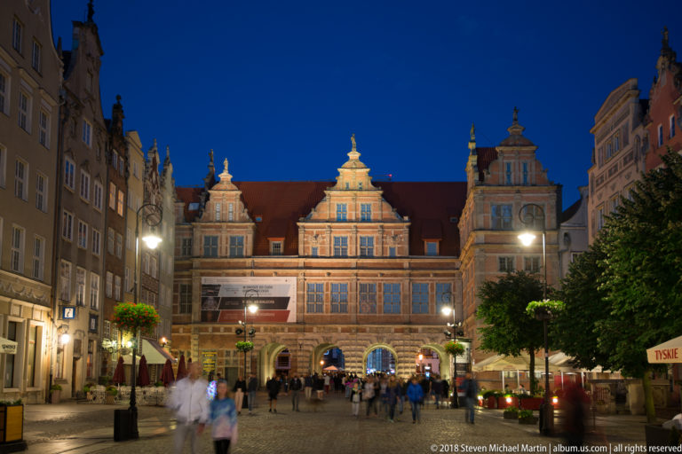 Illuminated Green Gate with ornate gables, tall windows, and multiple arched passages at the end of Długi Targ.