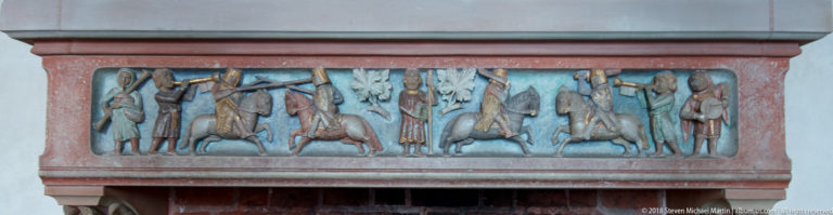 Rectangular painted relief with medieval-style figures, horses, trees, and muted blue, red, and ochre coloring.