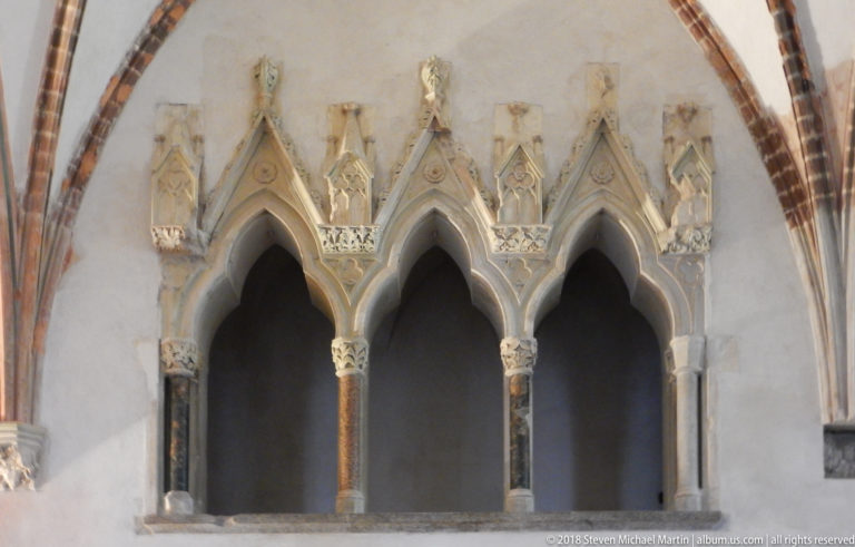 Three pointed Gothic arches on slender columns, with carved capitals and small figures in niches above.