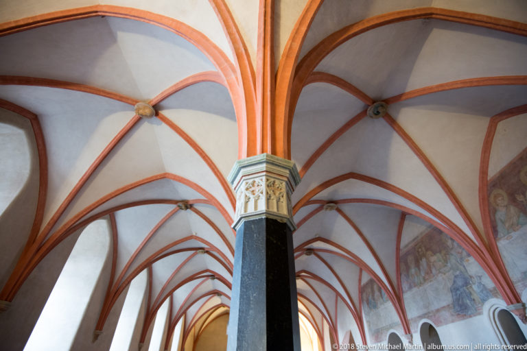 Red-painted Gothic ribs spring from a tall dark column with a decorated capital beneath pale vaulted ceilings.