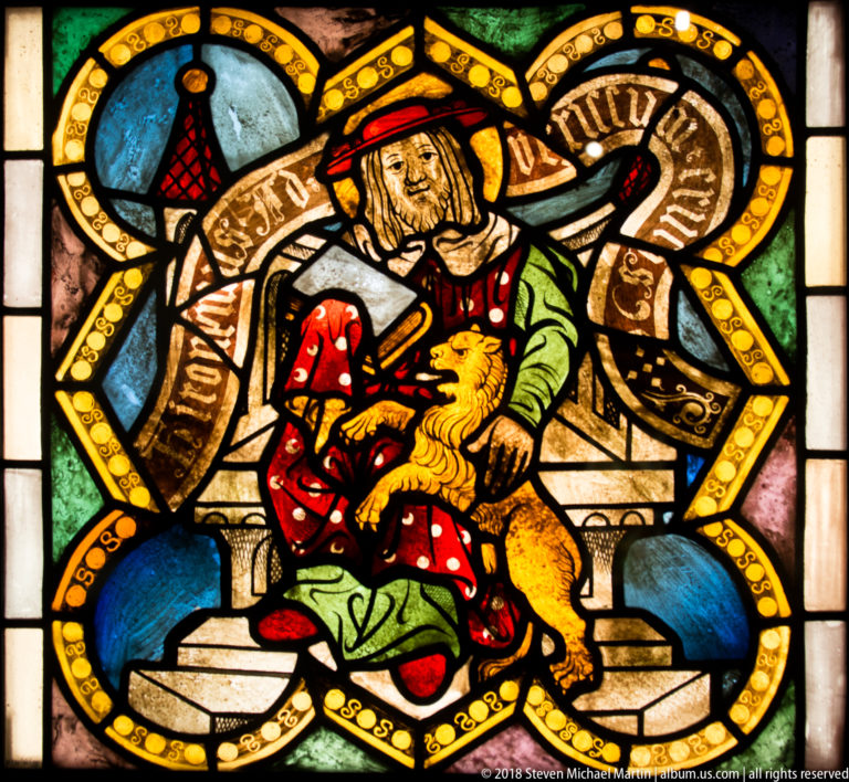 Saint Jerome seated with a book and his lion attribute in a stained-glass quatrefoil.