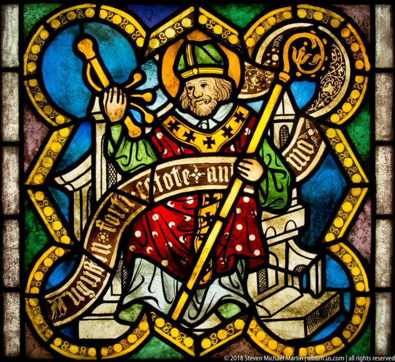 Saint Augustine of Hippo seated as a mitred bishop with crozier, raised hand, and inscribed scroll.