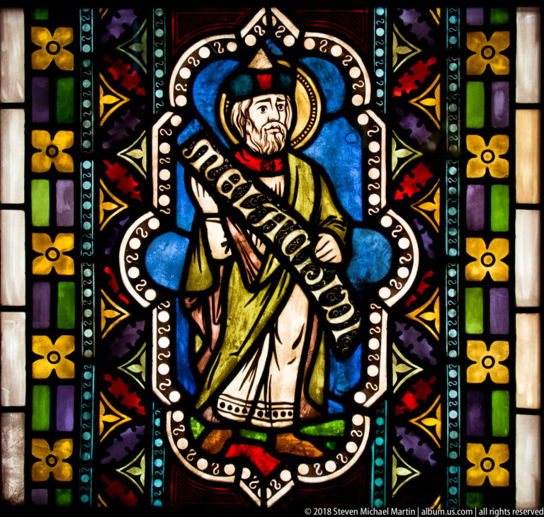 Saint Gregory the Great holding an inscribed scroll in a blue and multicolored Gothic-style stained-glass panel.