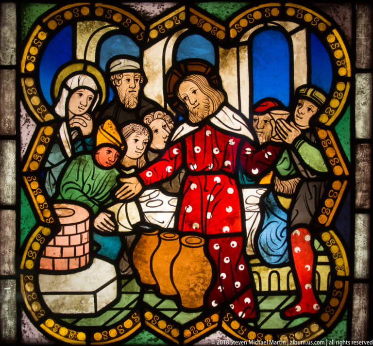 Haloed central figure in red robes surrounded by men and women beside a large rounded vessel in an interior.