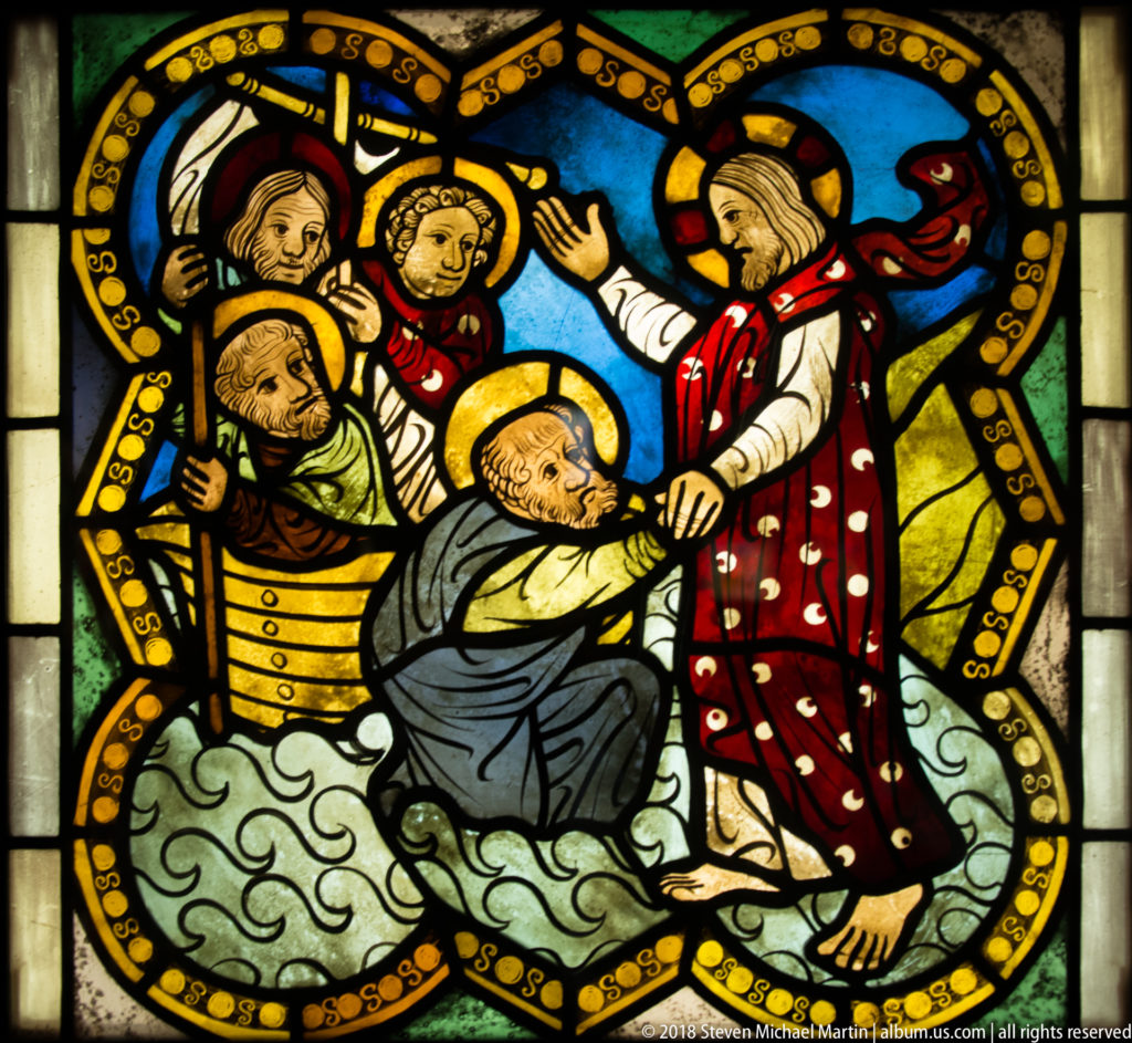 Christ grasping Saint Peter as he sinks amid stylized waves in a stained-glass Gospel scene.