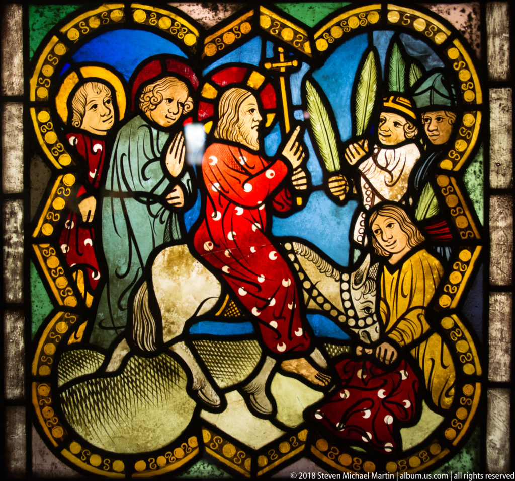 Christ riding a donkey into Jerusalem as figures greet him with palm branches.