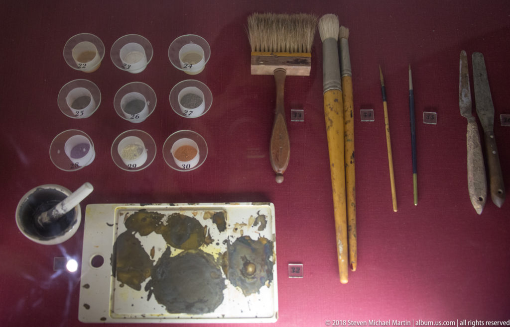 Brushes, pigment vessels, palette, and specialized hand tools displayed to explain painting and working stained glass.