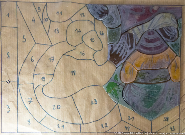Numbered full-size stained-glass cartoon beside corresponding cut and painted glass pieces forming part of a figure.