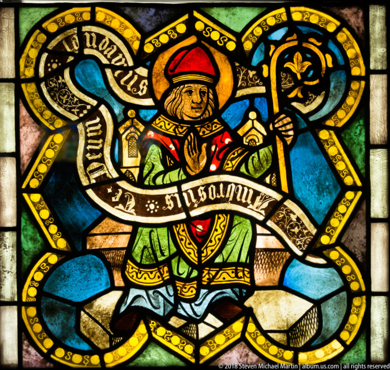 Saint Ambrose of Milan seated in episcopal vestments with mitre, crozier, and inscribed scroll.