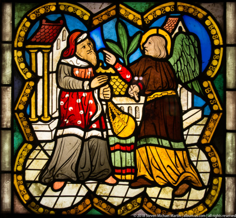 Winged angel standing between two kneeling figures in red and brown garments within a medieval stained-glass scene.
