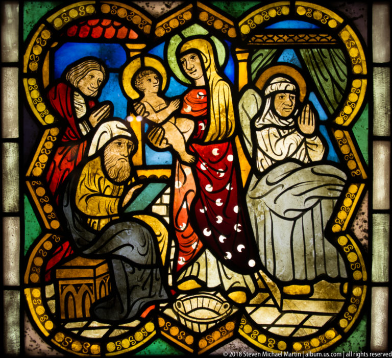 Group scene with seated elder, woman and haloed child, and a curtained bed in a stained-glass interior.