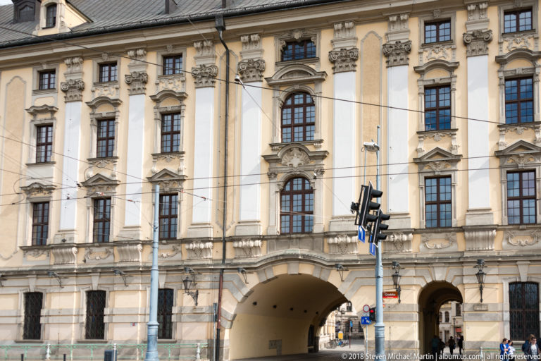Tall Baroque university façade with sculpted window surrounds and a large arched passage opening onto the street.