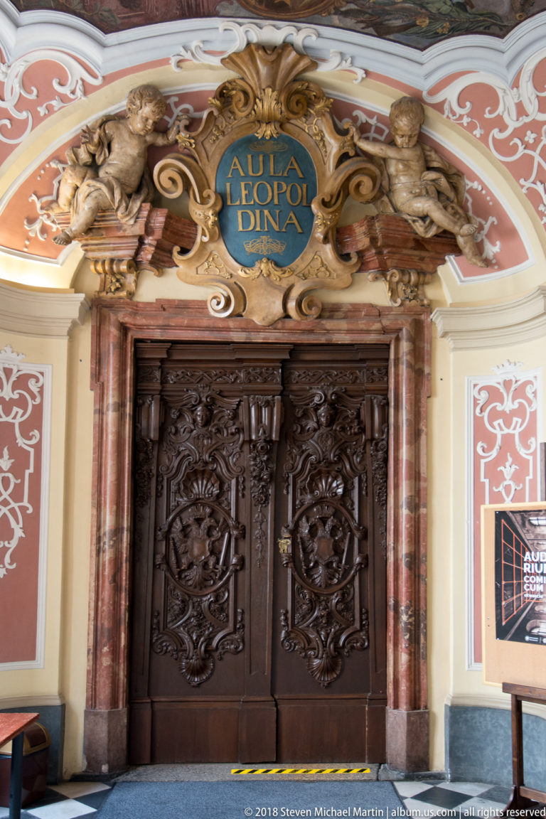 Frontal view of the Aula Leopoldina carved double doors, marbleized columns, gilded figures, and blue name cartouche.
