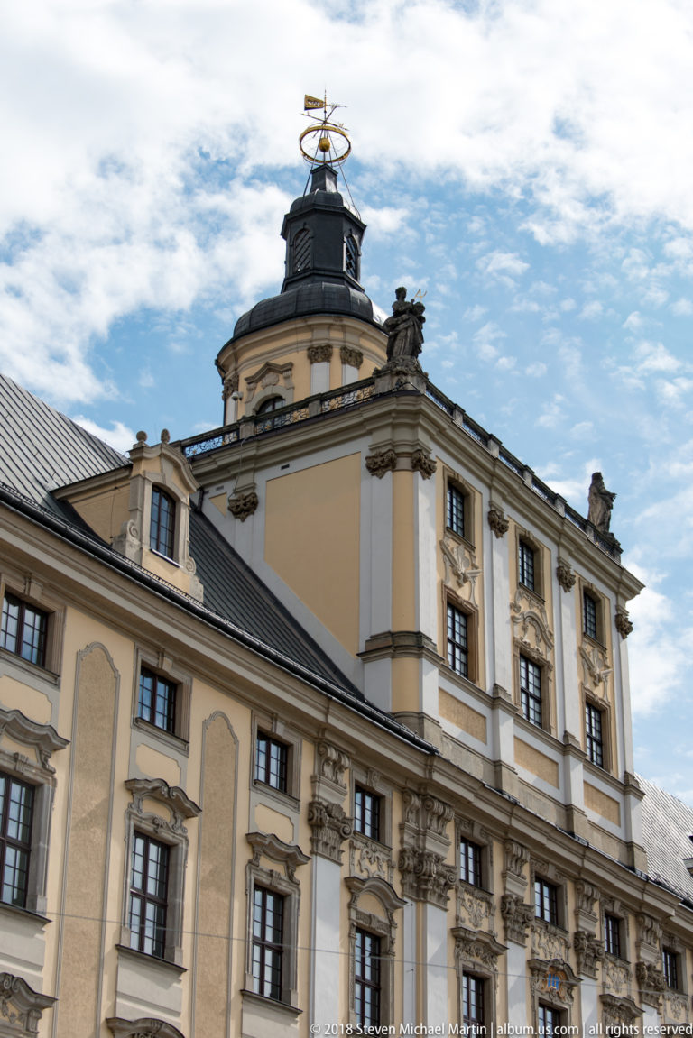 Baroque university corner pavilion with dark roof and openwork astronomical ornament rising above rows of decorated windows.
