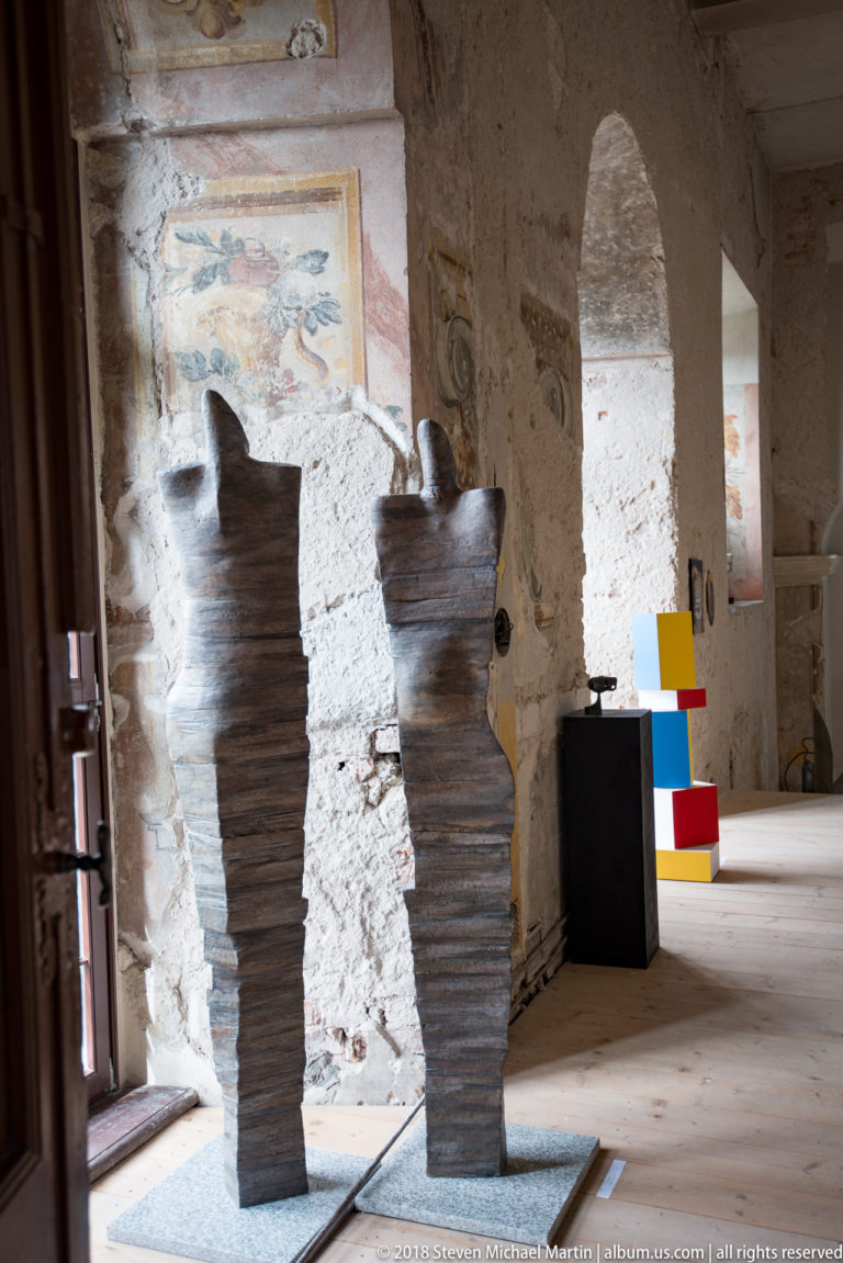 Two tall dark ribbed sculptural vessels beside a doorway in a gallery with exposed historic walls.