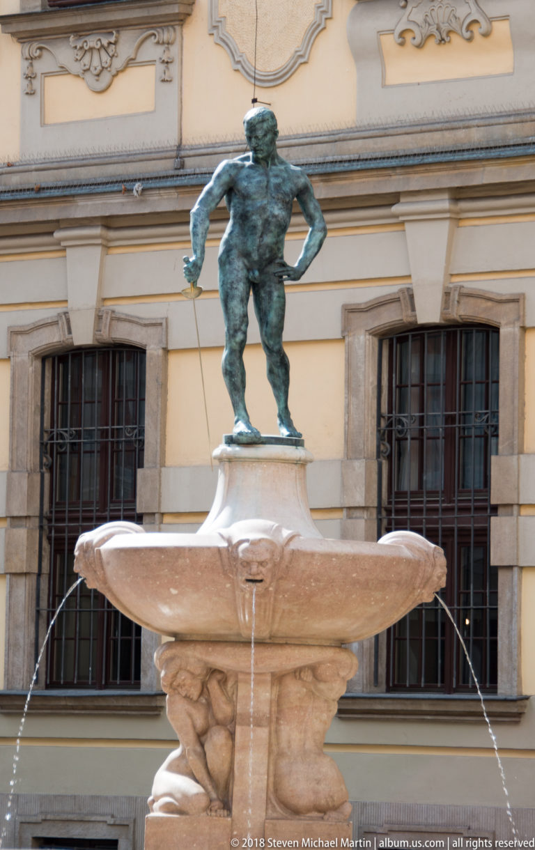 Bronze nude fencer standing atop a stone fountain basin in front of the University of Wrocław.