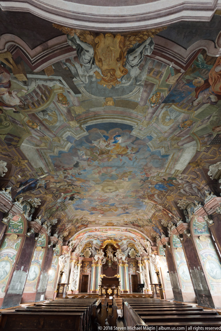 Wide-angle rear view of Aula Leopoldina with rows of seating beneath an expansive frescoed ceiling and distant ceremonial dais.