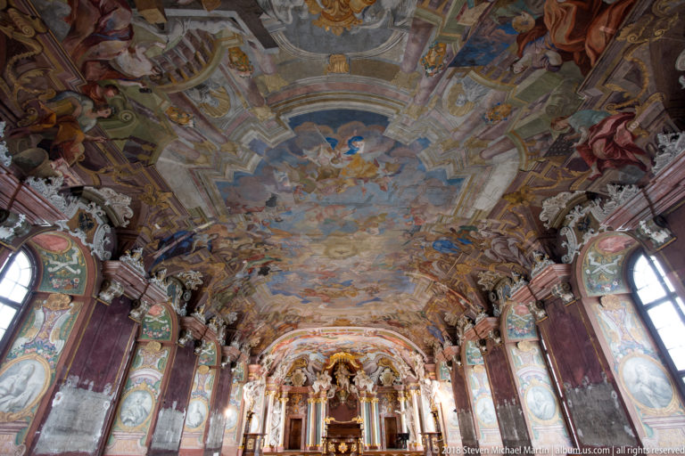 Long interior view of Aula Leopoldina with frescoed ceiling, tall windows, philosopher panels, marbled columns, and ceremonial dais.