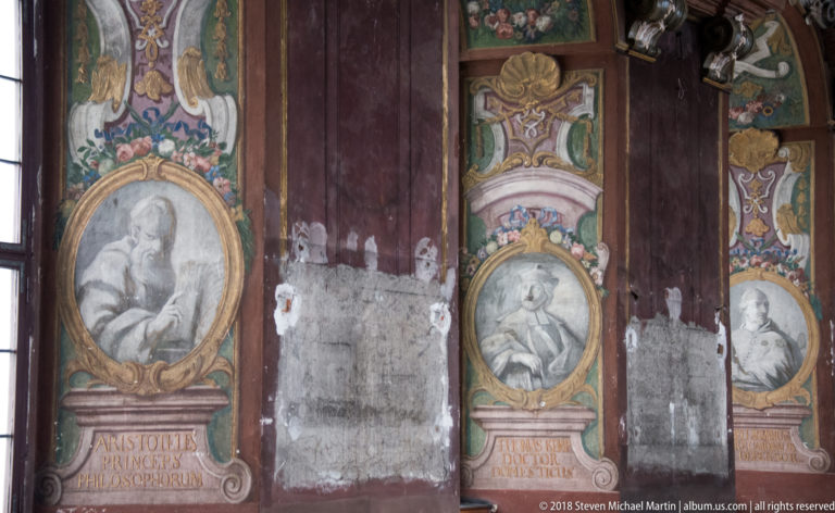 Aula Leopoldina wall panels with oval philosopher portraits, including Aristotle labeled in Latin, separated by worn painted surfaces.