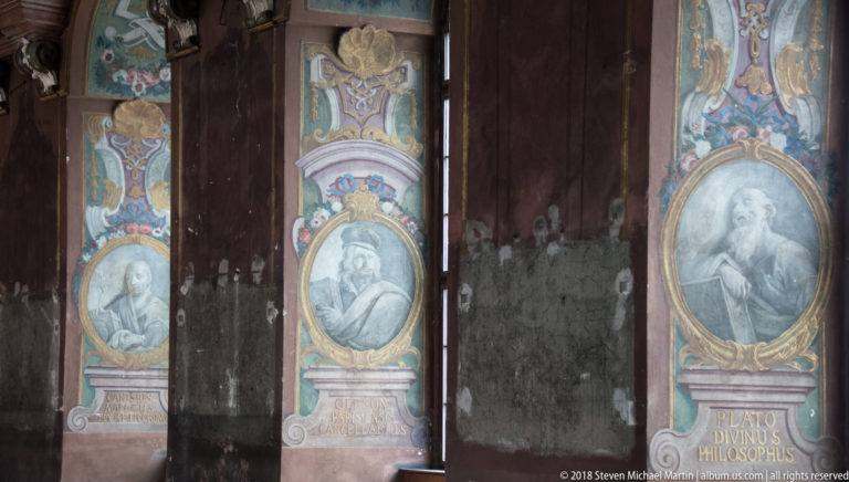 Painted wall panels with oval philosopher portraits; the right panel is labeled “PLATO DIVINUS PHILOSOPHUS,” with worn wall surfaces between.