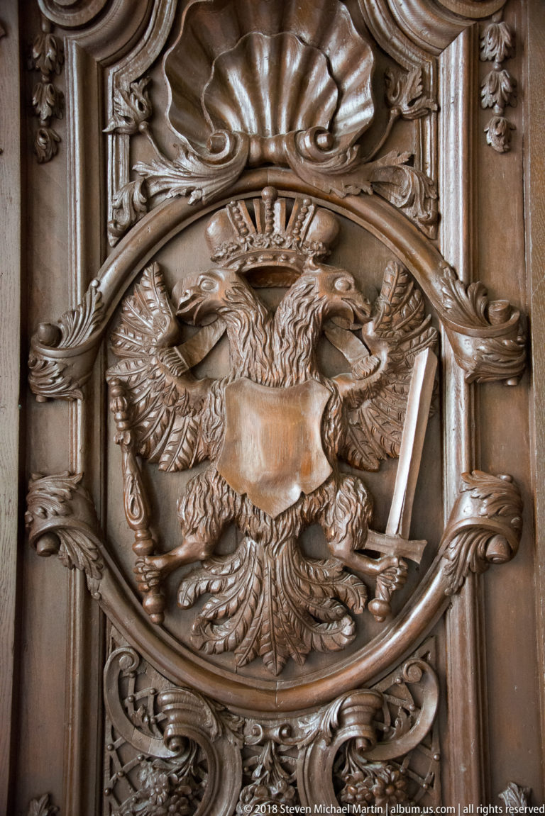 Dark carved wooden panel with a crowned double-headed eagle, central shield, spread wings, and surrounding foliage.