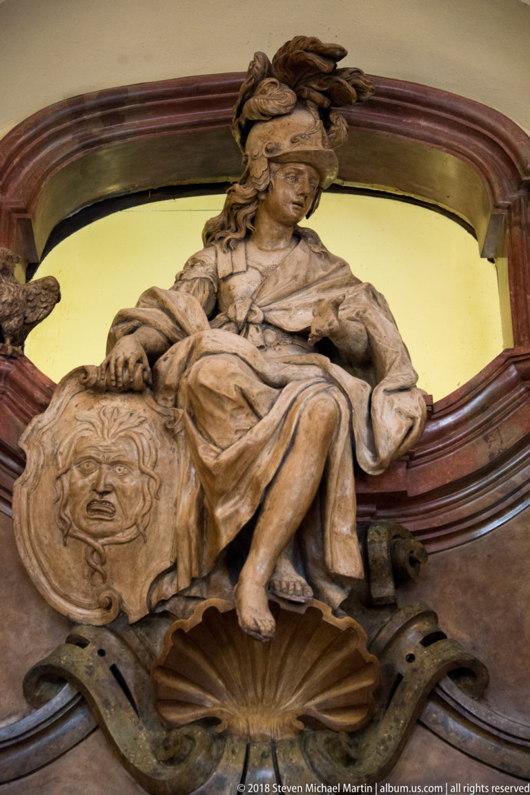Carved seated female figure with a large emblematic shield above shell and scroll ornament on an interior doorway.