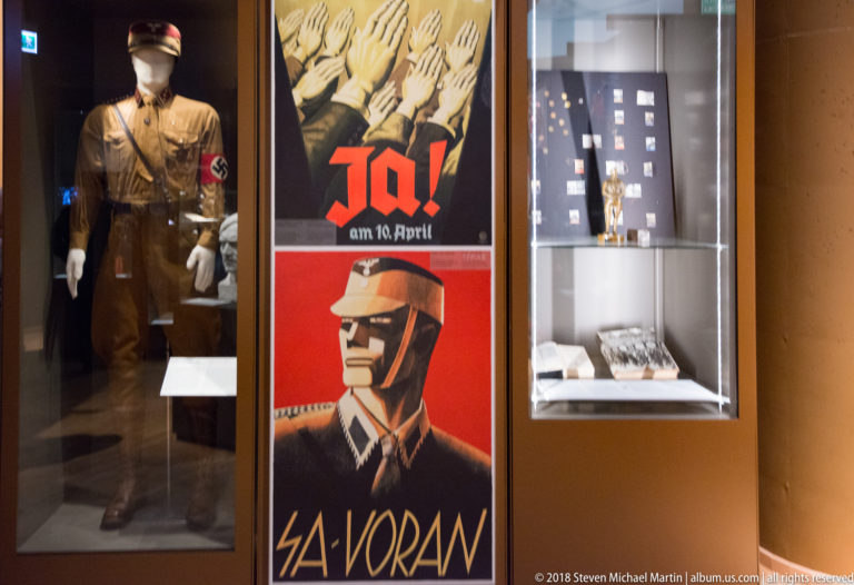 Brown uniformed mannequin beside red German propaganda posters reading Ja! and showing a stylized SA figure.