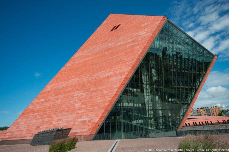 Close exterior view of the museum’s steep red-clad tower with a large triangular glass façade.