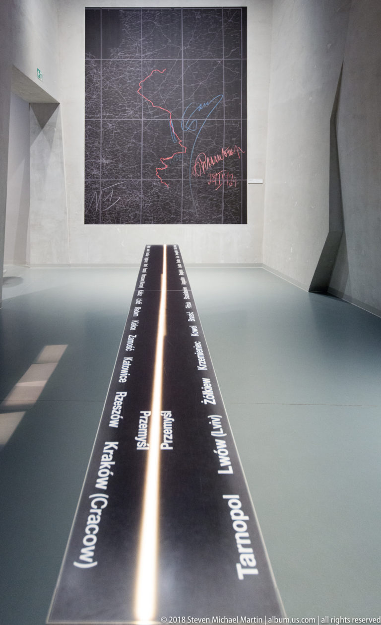 Illuminated floor timeline with place names leading toward a large annotated military map on the wall.