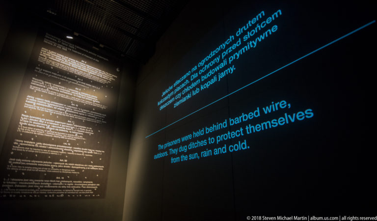 Blue bilingual text about prisoners behind barbed wire beside a large illuminated legal document.